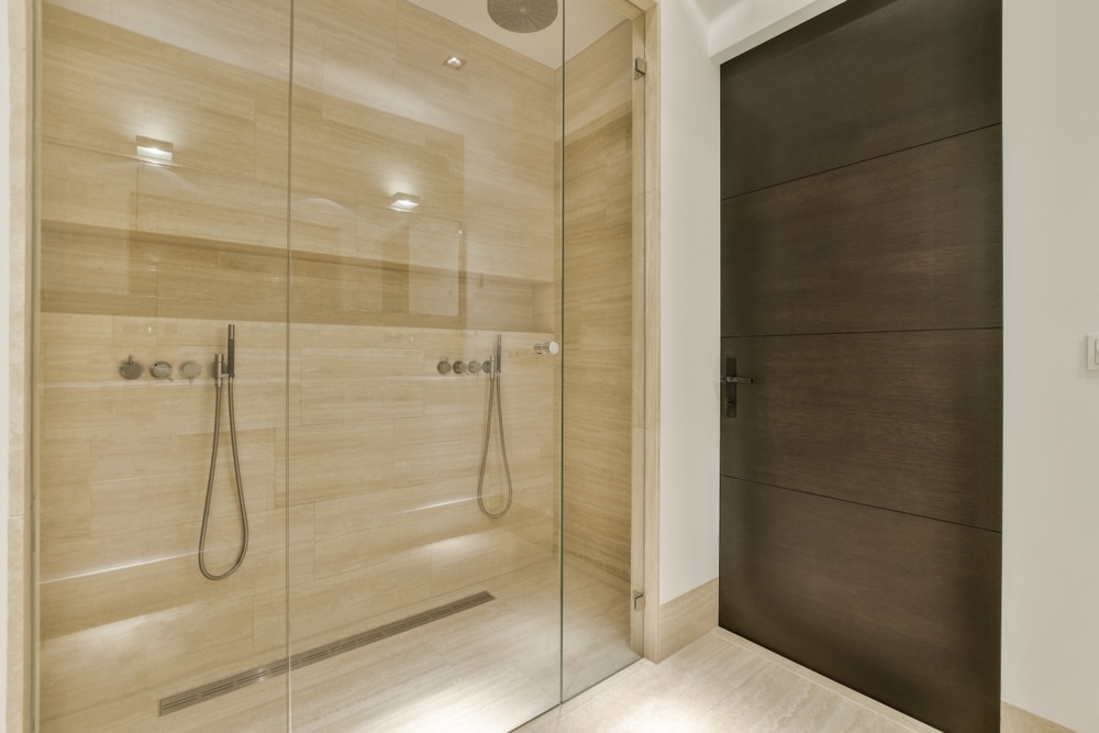 Douche moderne en pierre beige avec double pommeau et paroi en verre.